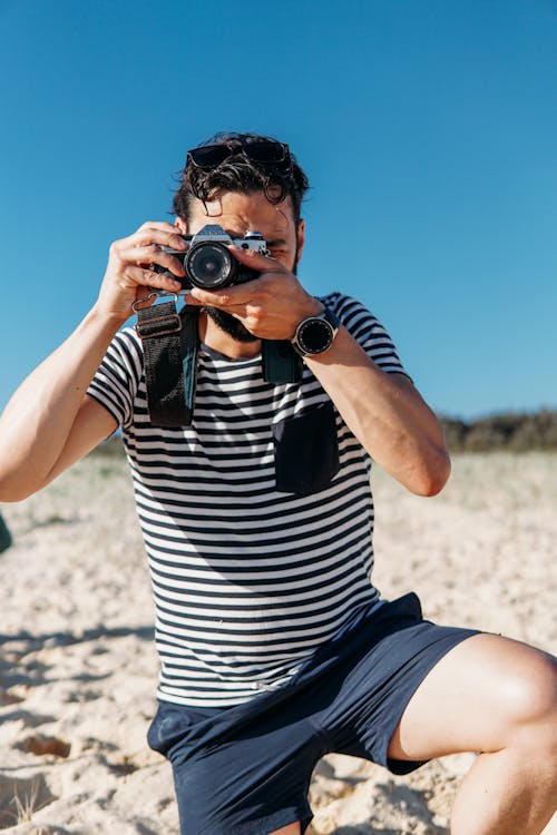 A Man in Striped Shirt Using DSLR Camera while on the Beach