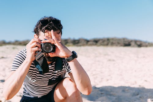 Free A Man in Striped Shirt Using DSLR Camera while on the Beach Stock Photo