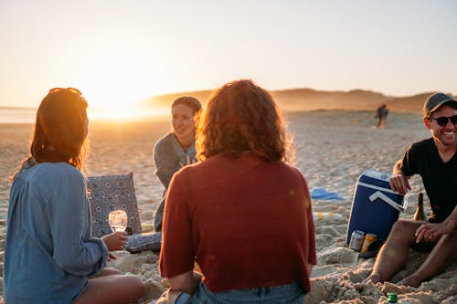 People Drinking while Sitting on the Beach During Sunset