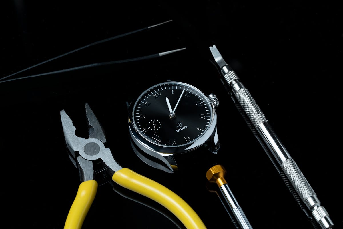 Pinzette e micro-cacciaviti per orologeria disposti su sfondo scuro