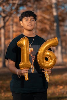 Teen holding gold number balloons outdoors on a sunny day, celebrating a birthday.