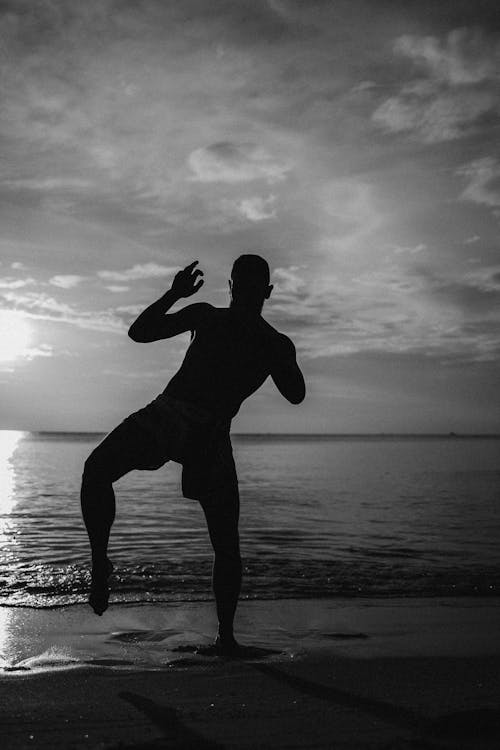 Silhouette of Man Practicing Kickboxing on the Seashore During Sunset
