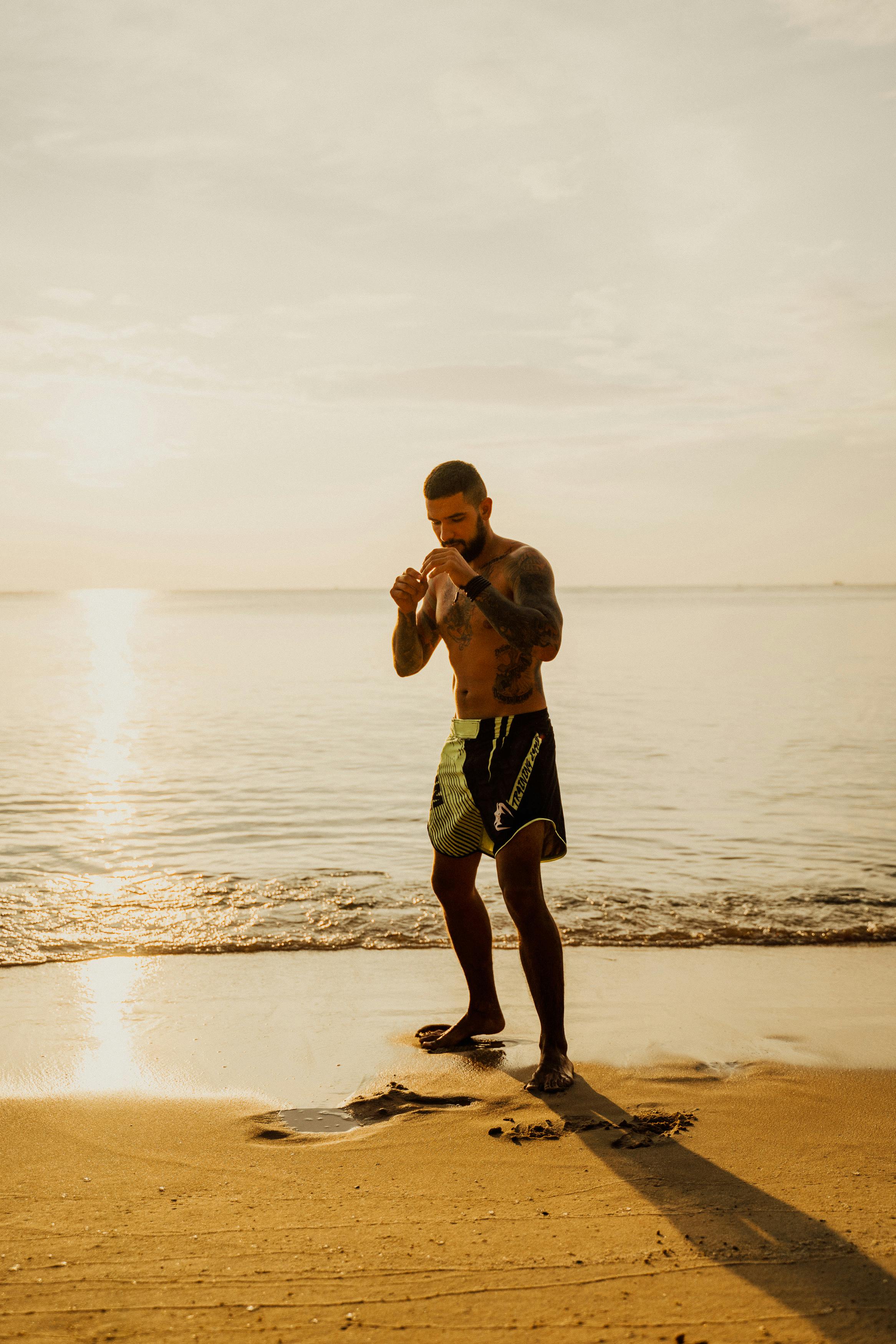 man in black shorts standing on the seashore during sunset