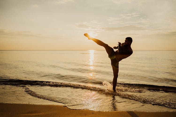 A Man Practicing Kick Boxing While On The Seashore