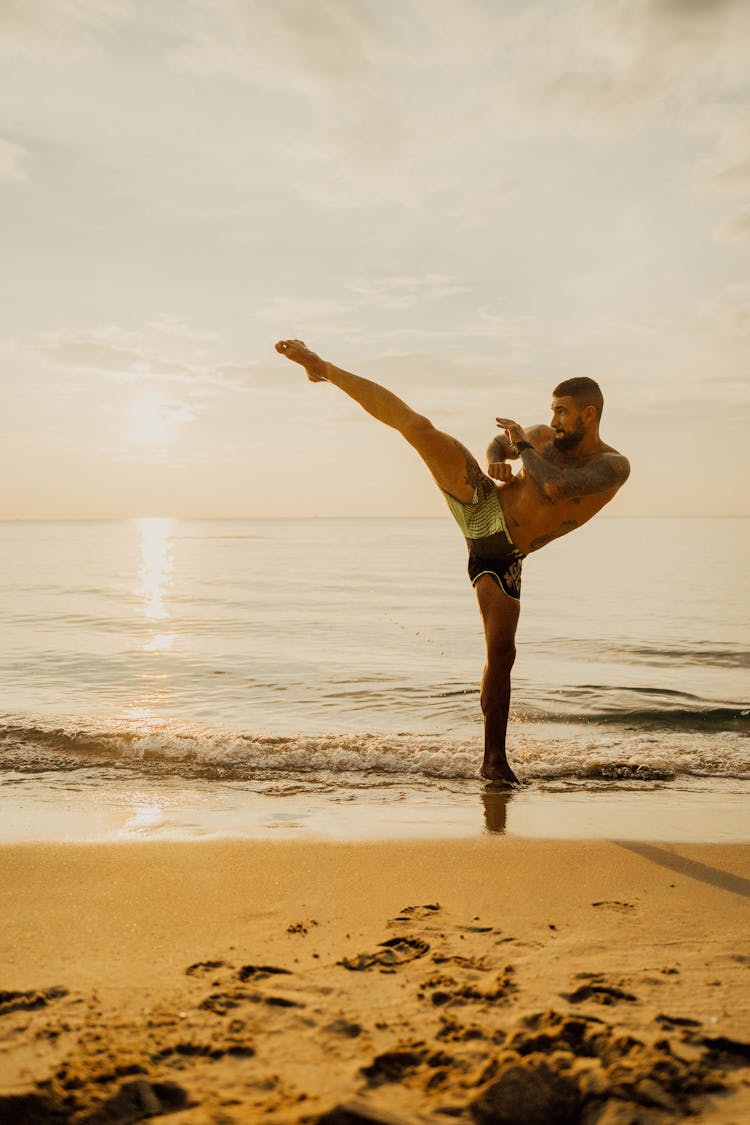 A Man Practicing Kick Boxing While On The Seashore