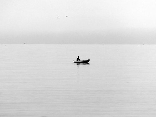 Free A solitary person rowing a boat on a serene, grayscale ocean under an expansive sky. Stock Photo