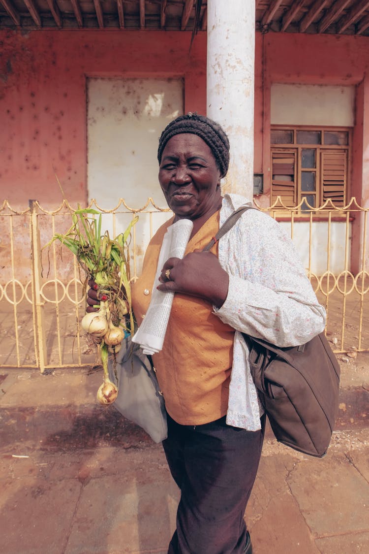 Cheerful Black Woman With Onions In Hand Standing On Street