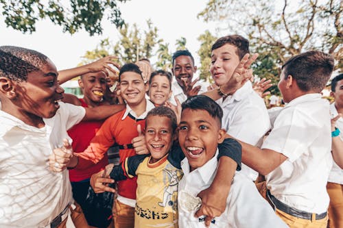 Group of cheerful delighted diverse boys wearing casual clothes gathering on sunny street and laughing while hugging each other