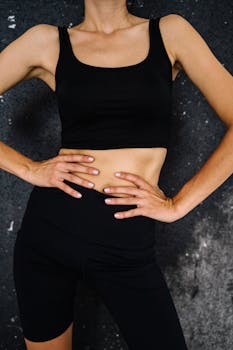 Close-up of a woman's torso in black activewear with hands on waist against dark background.
