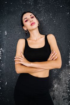 一位自信的女性身着黑色运动服，在质感背景前摆出姿势，散发着力量感
