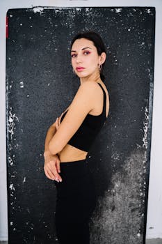 Portrait of a confident woman in black active wear standing with arms crossed against a textured backdrop.