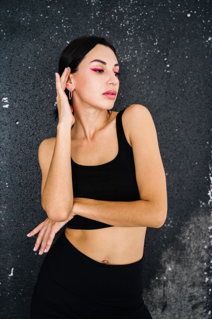Confident woman in active wear posing against textured wall with stylish makeup.