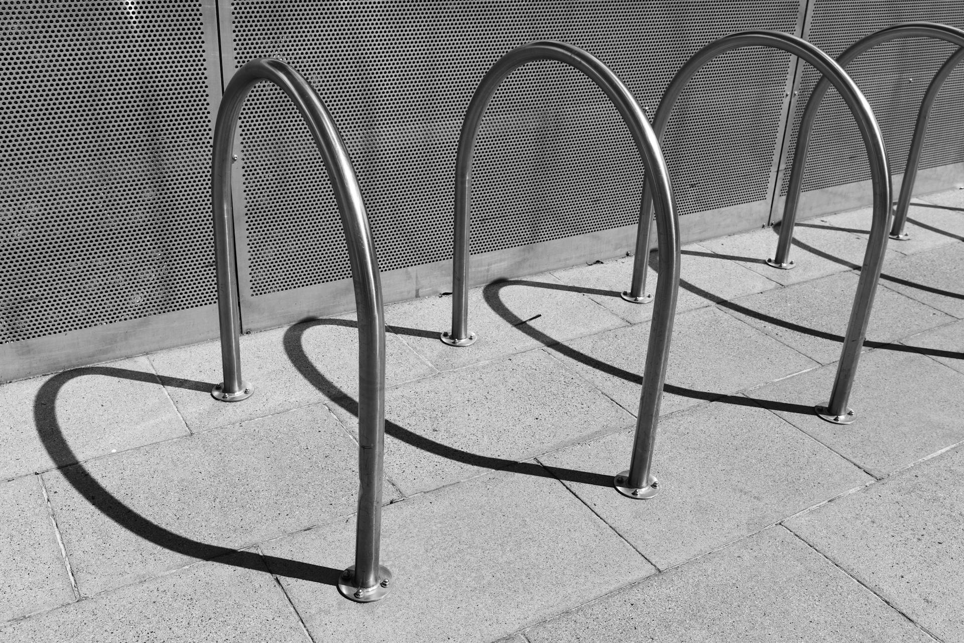 Minimalist steel bicycle rack casting shadows on pavement in city.