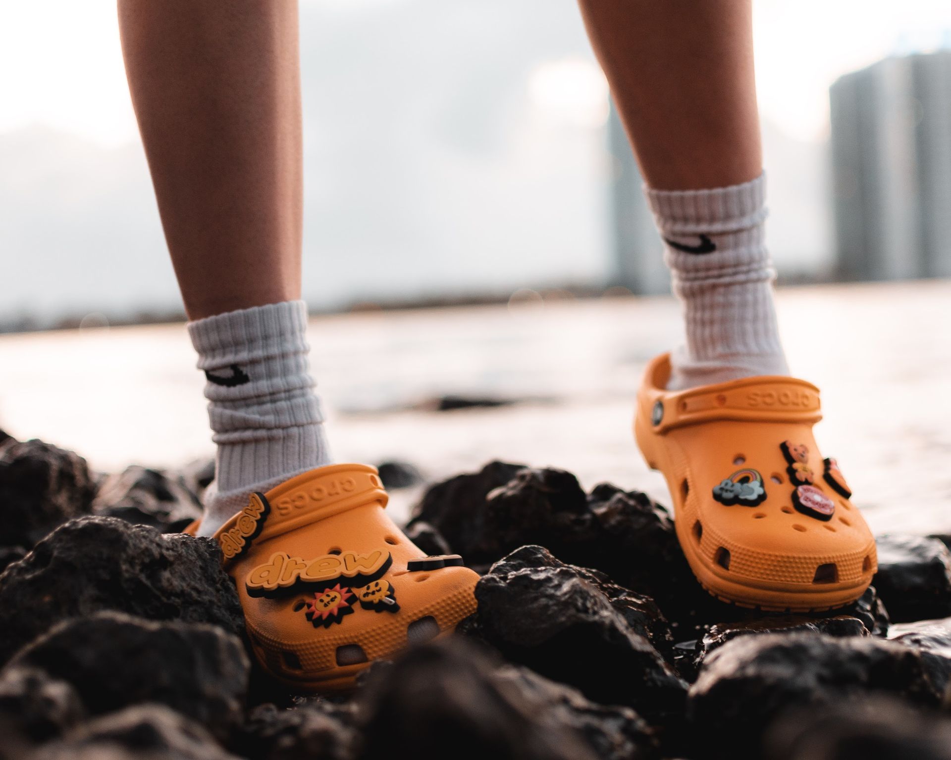 Close-up of legs wearing yellow Crocs with white socks on rocky beach.