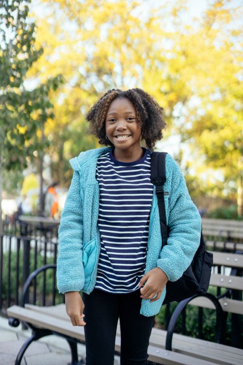 Free Cheerful African American child in casual clothes with Afro hairstyle and backpack smiling while spending time in park Stock Photo
