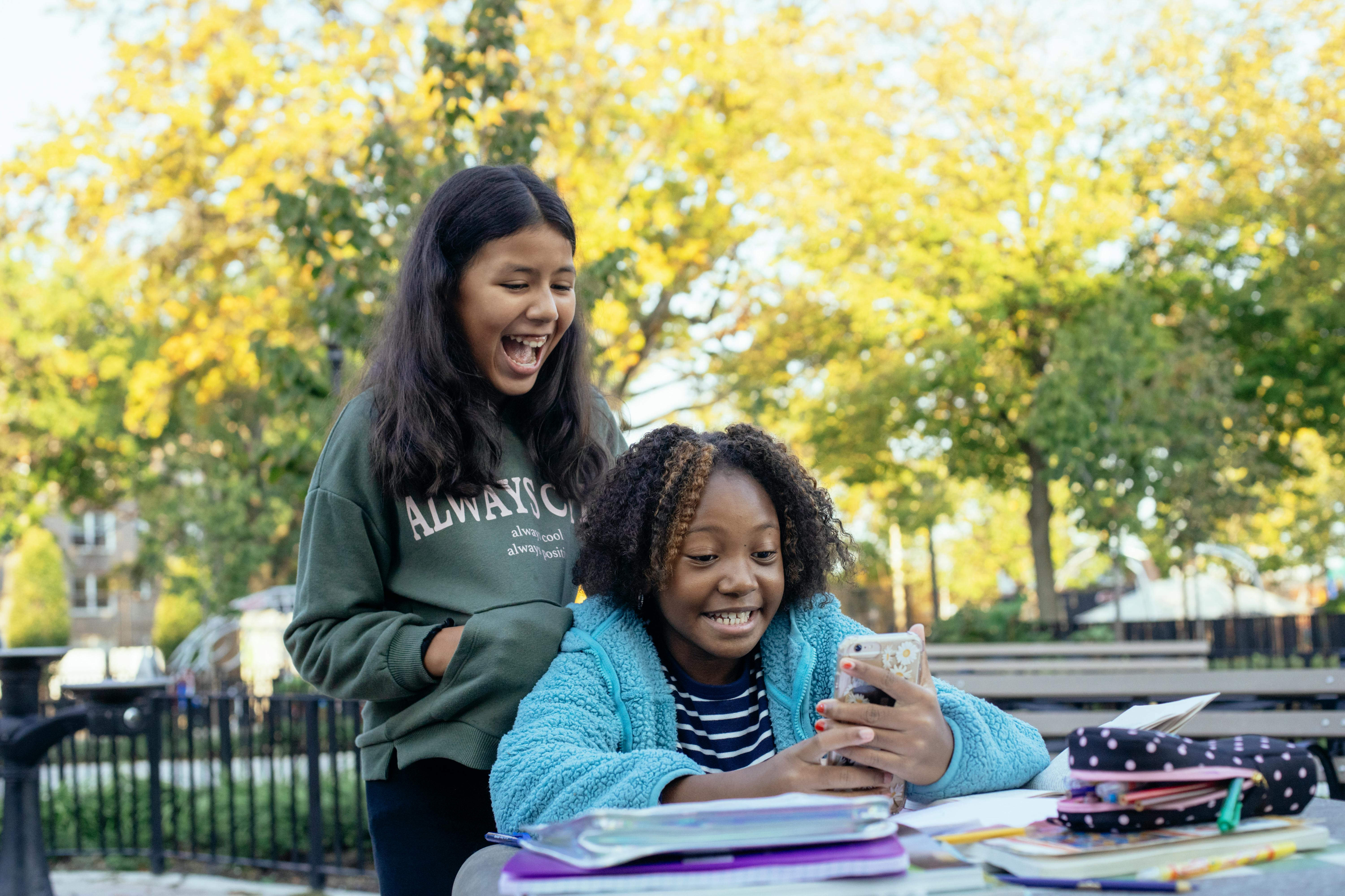 cheerful diverse classmates browsing smartphone and laughing