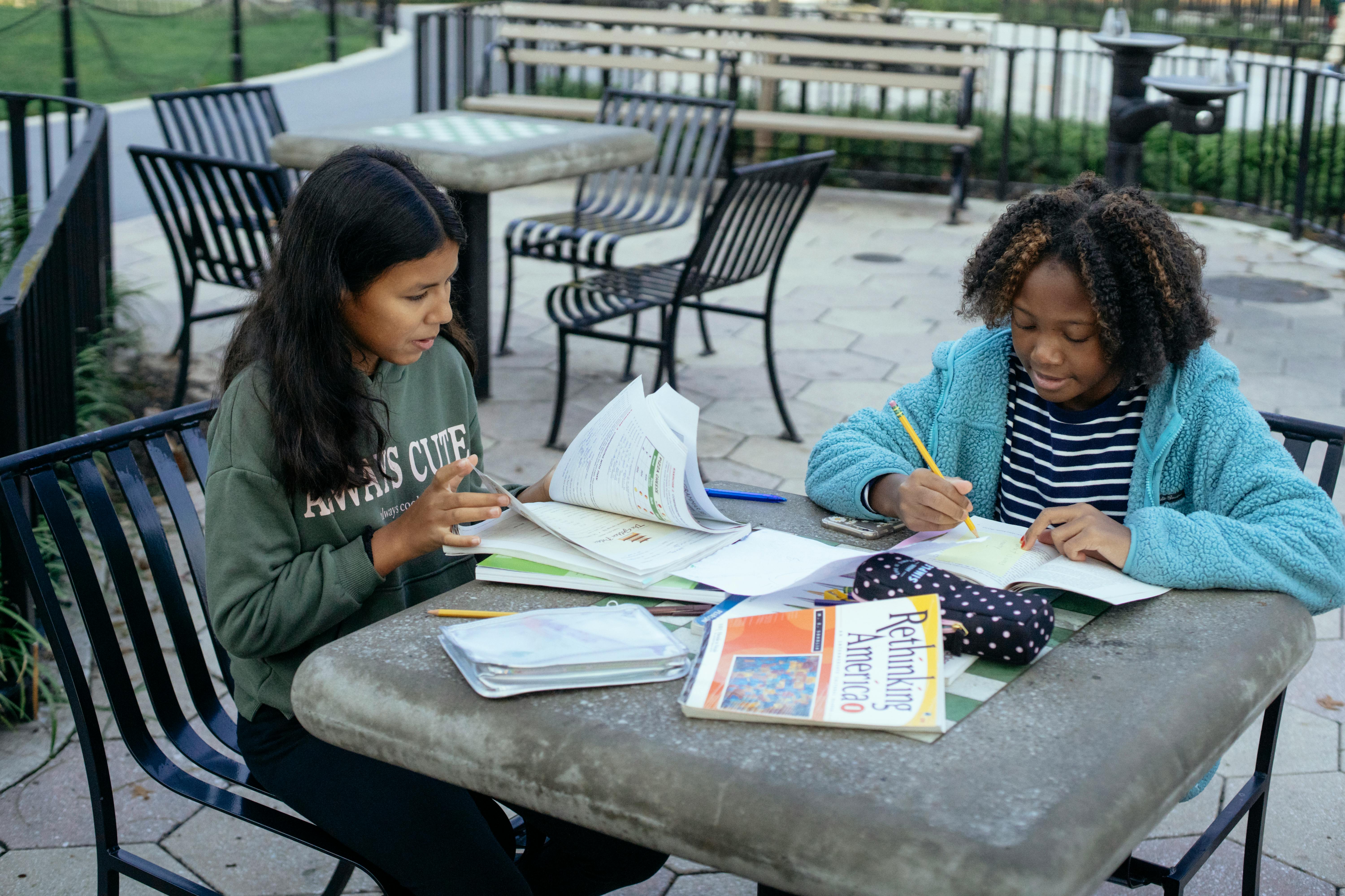 focused multiethnic schoolgirls doing homework in park