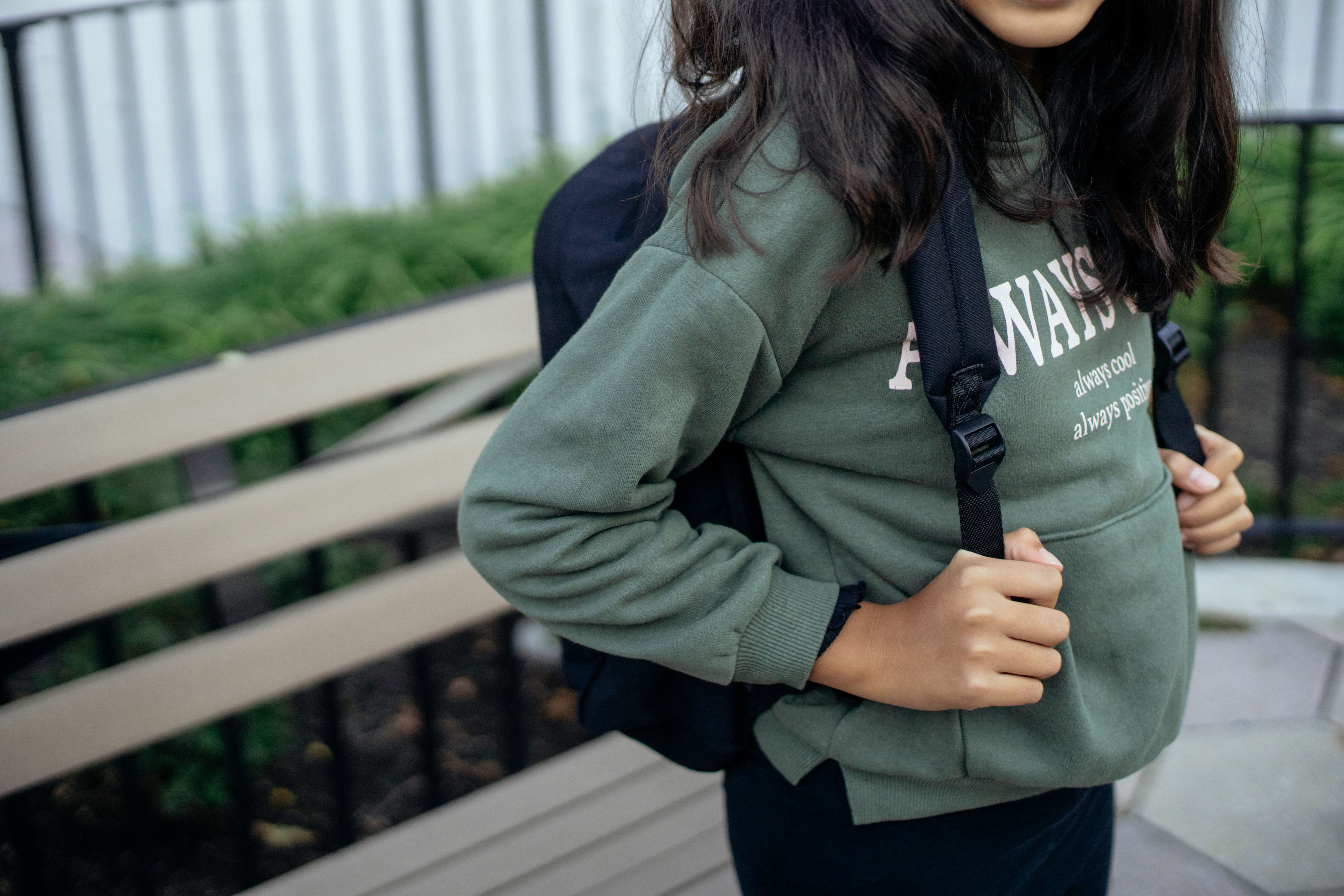 一名穿着休闲服、背着背包的无脸女学生站在城市公园的木凳附近