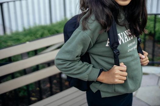一名穿着休闲服、背着背包的无脸女学生站在城市公园的木凳附近