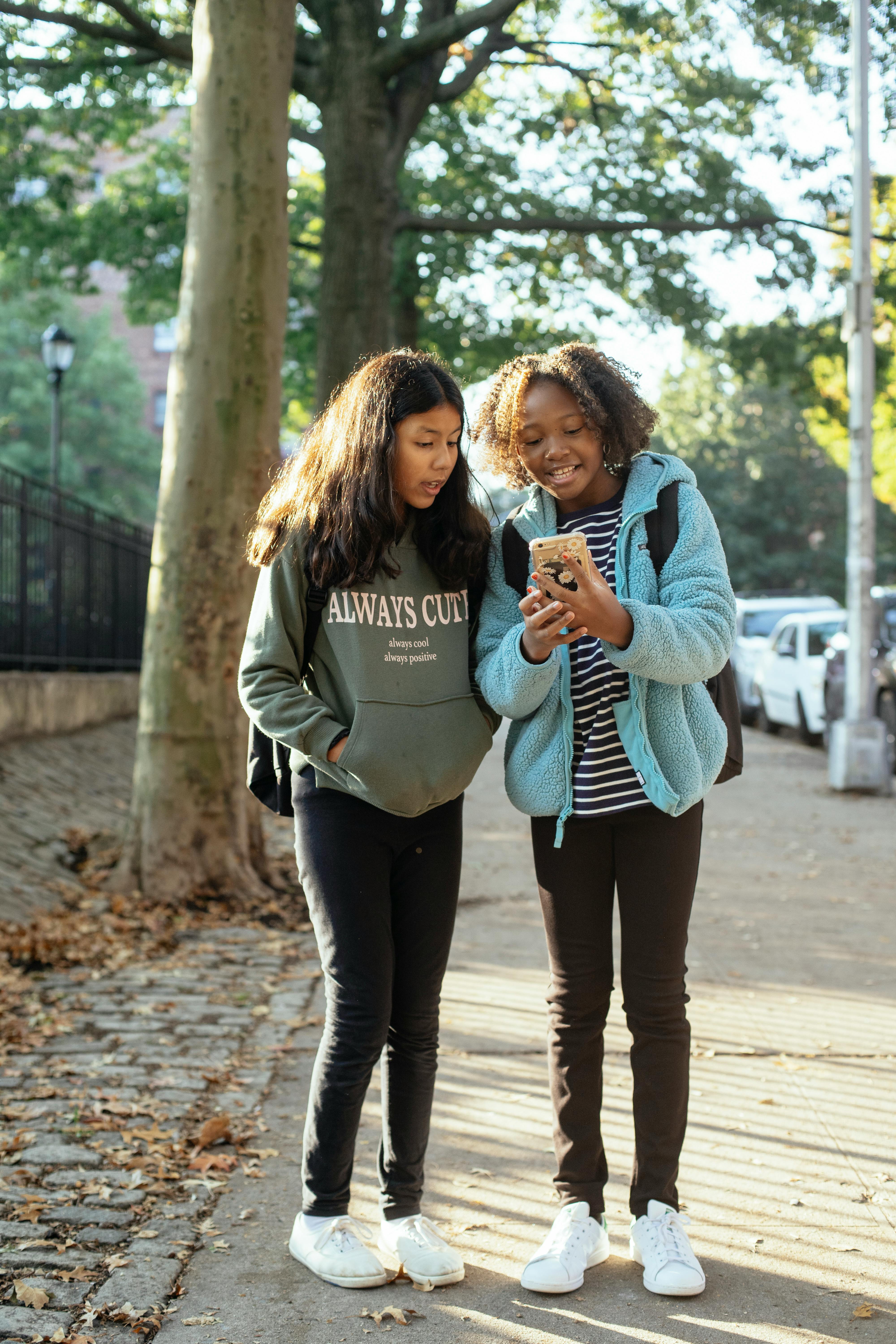 cheerful schoolgirls with smartphone on sidewalk