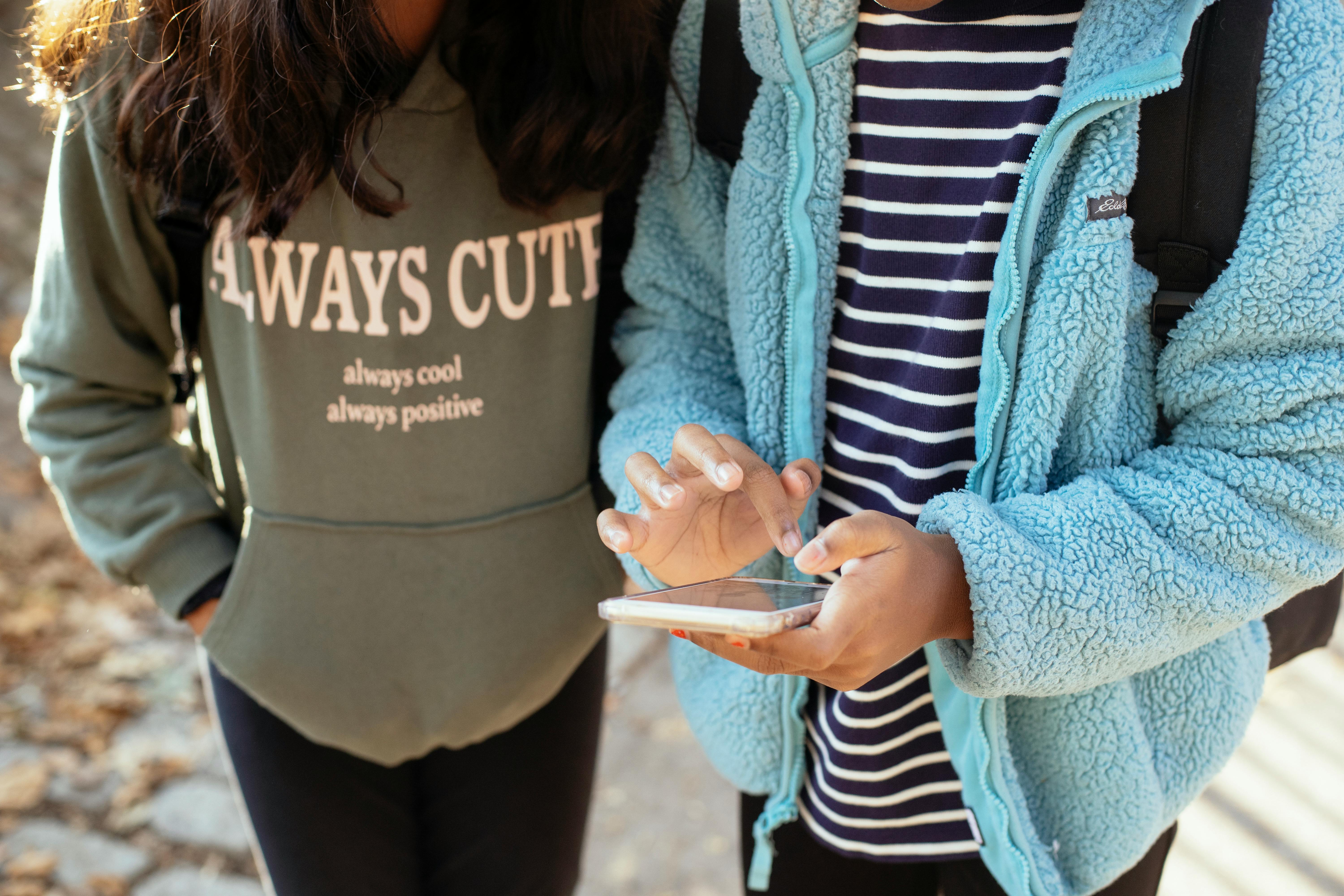 crop ethnic classmates with smartphone in park