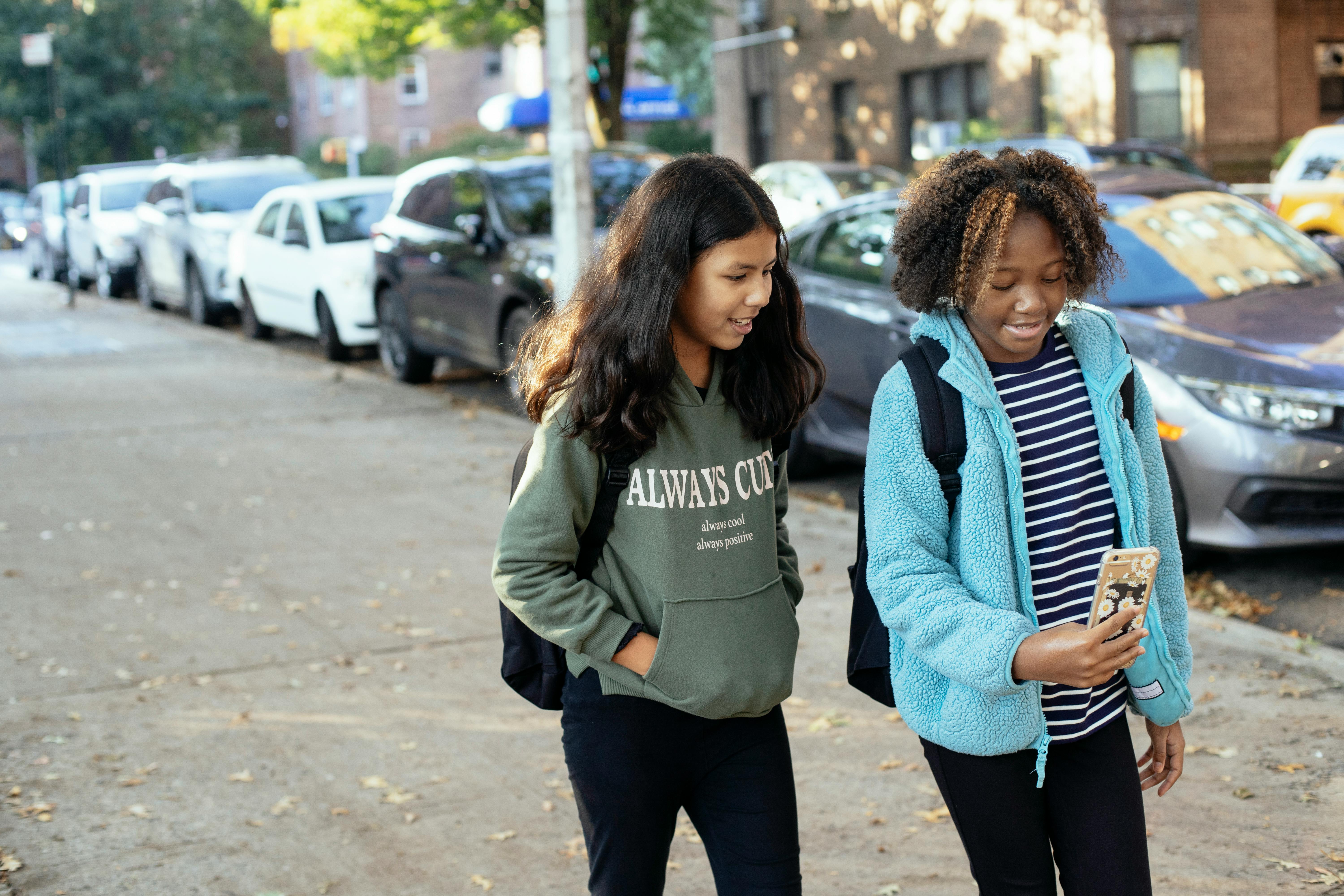 happy diverse girlfriends walking on street with smartphone