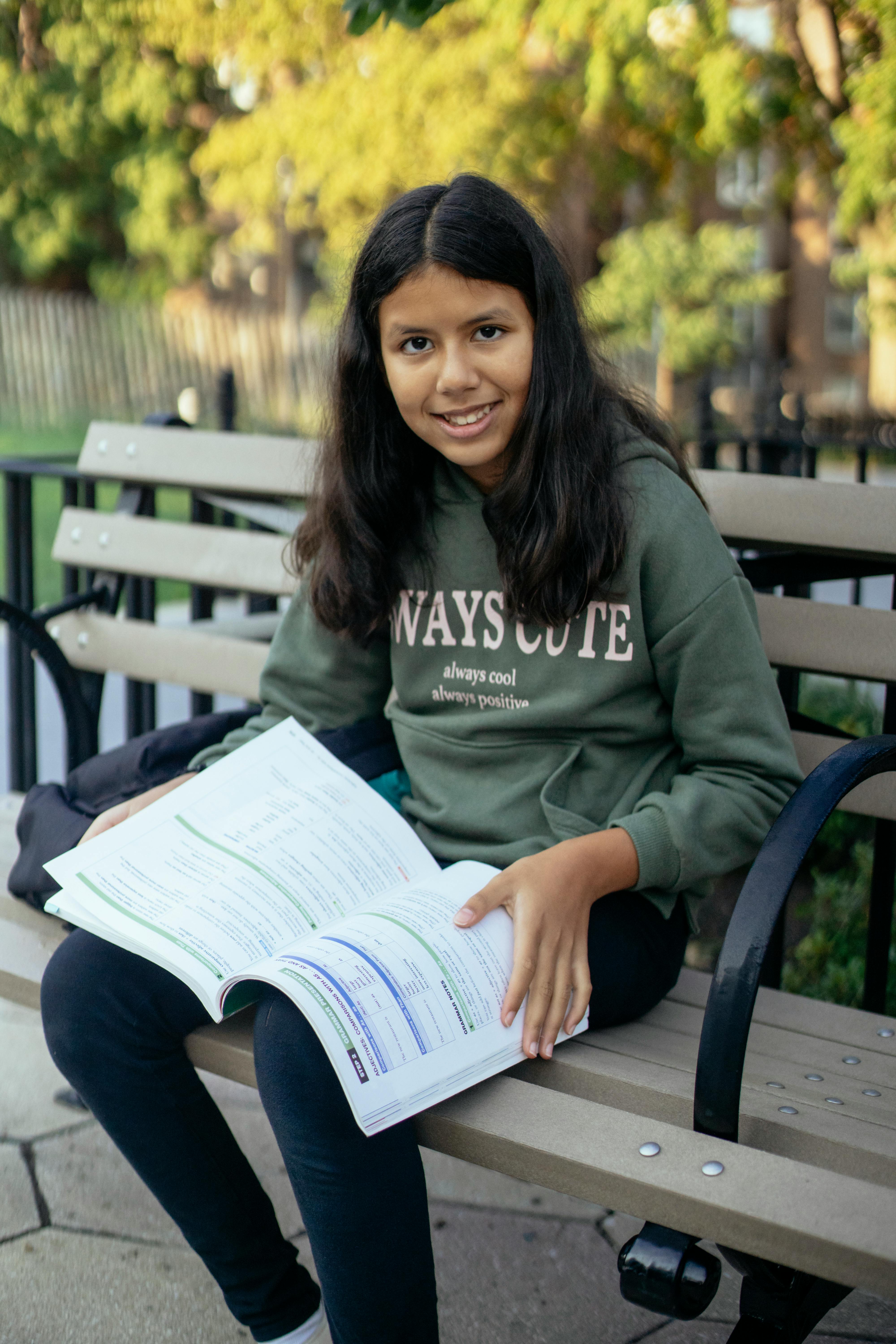 smiling little girl with textbook in park