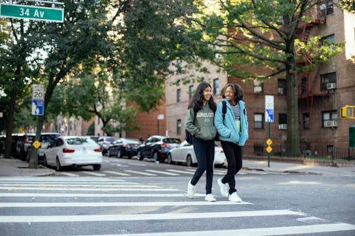 Cheerful schoolgirls crossing road in city