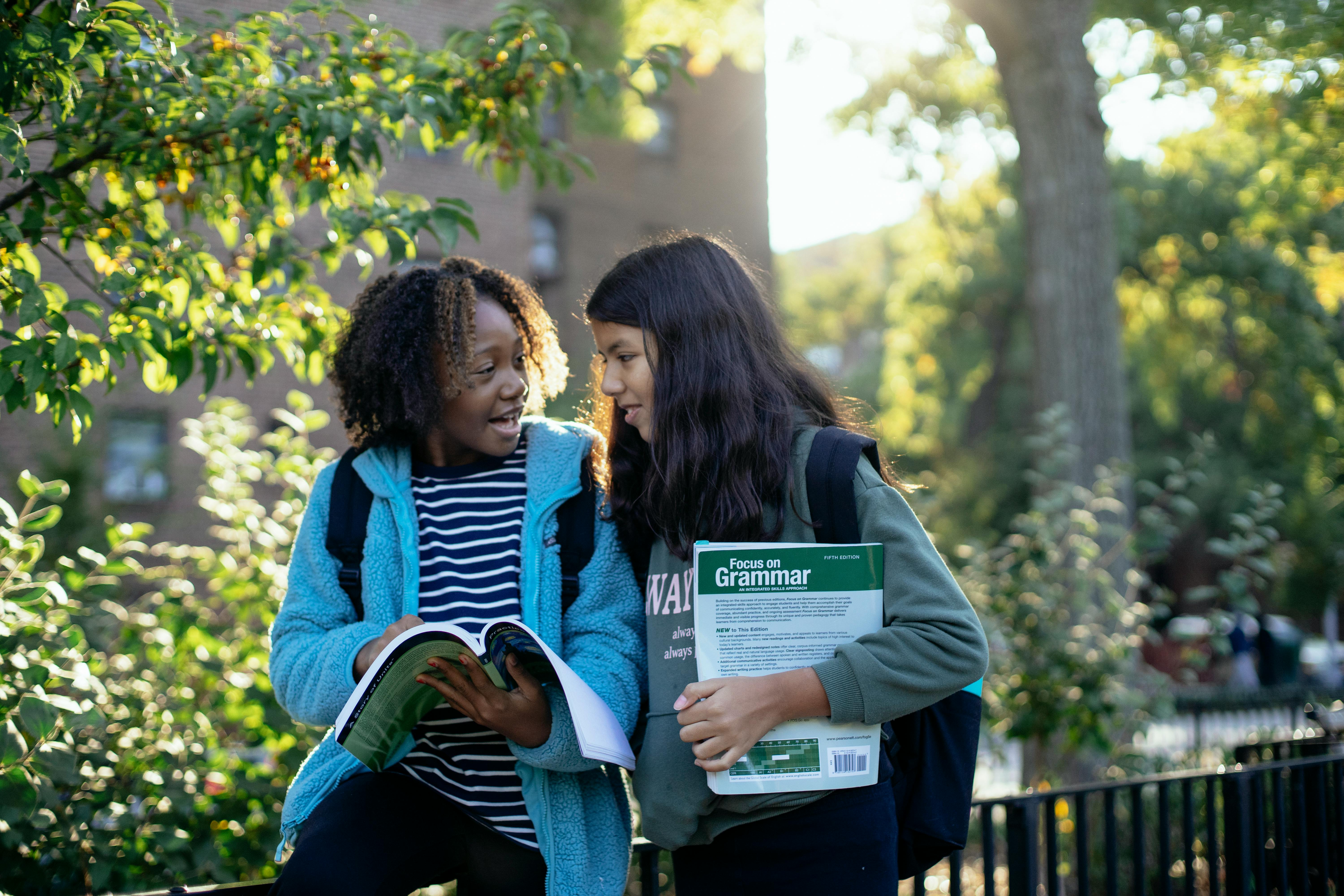 happy schoolgirls studying together in park