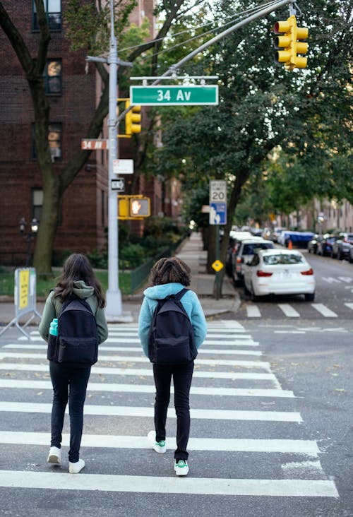 Unrecognizable schoolgirls with backpacks crossing city road