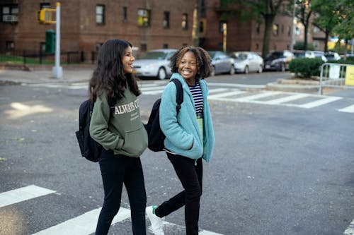 Happy multiethnic girlfriends with backpacks speaking on city road