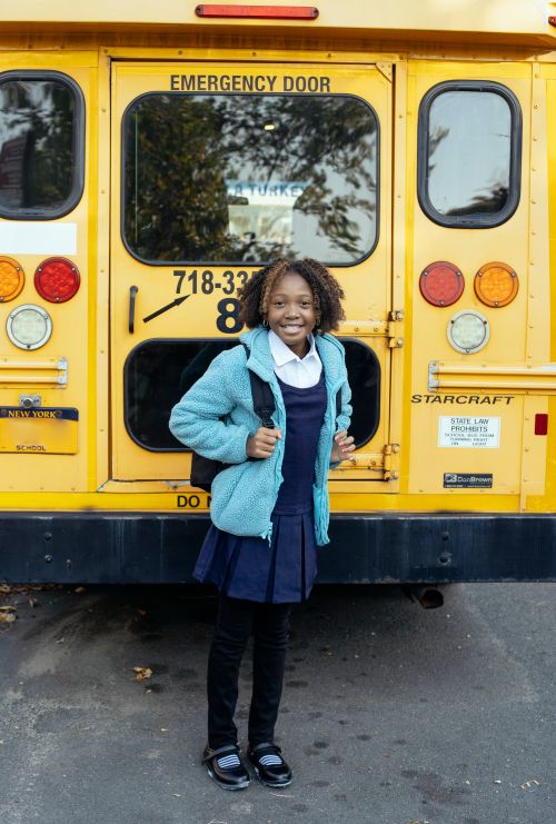 Free Content African American schoolkid in uniform looking at camera near bright bus on urban asphalt roadway Stock Photo