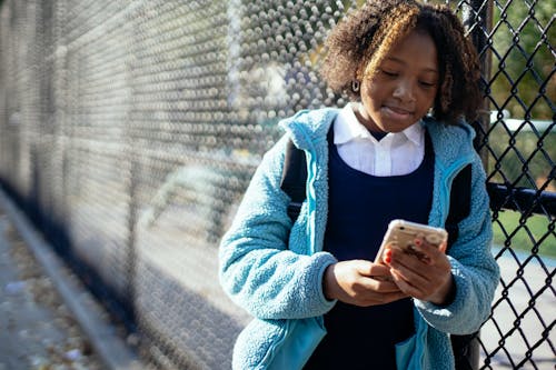 Free Cheerful black schoolgirl using smartphone on street Stock Photo