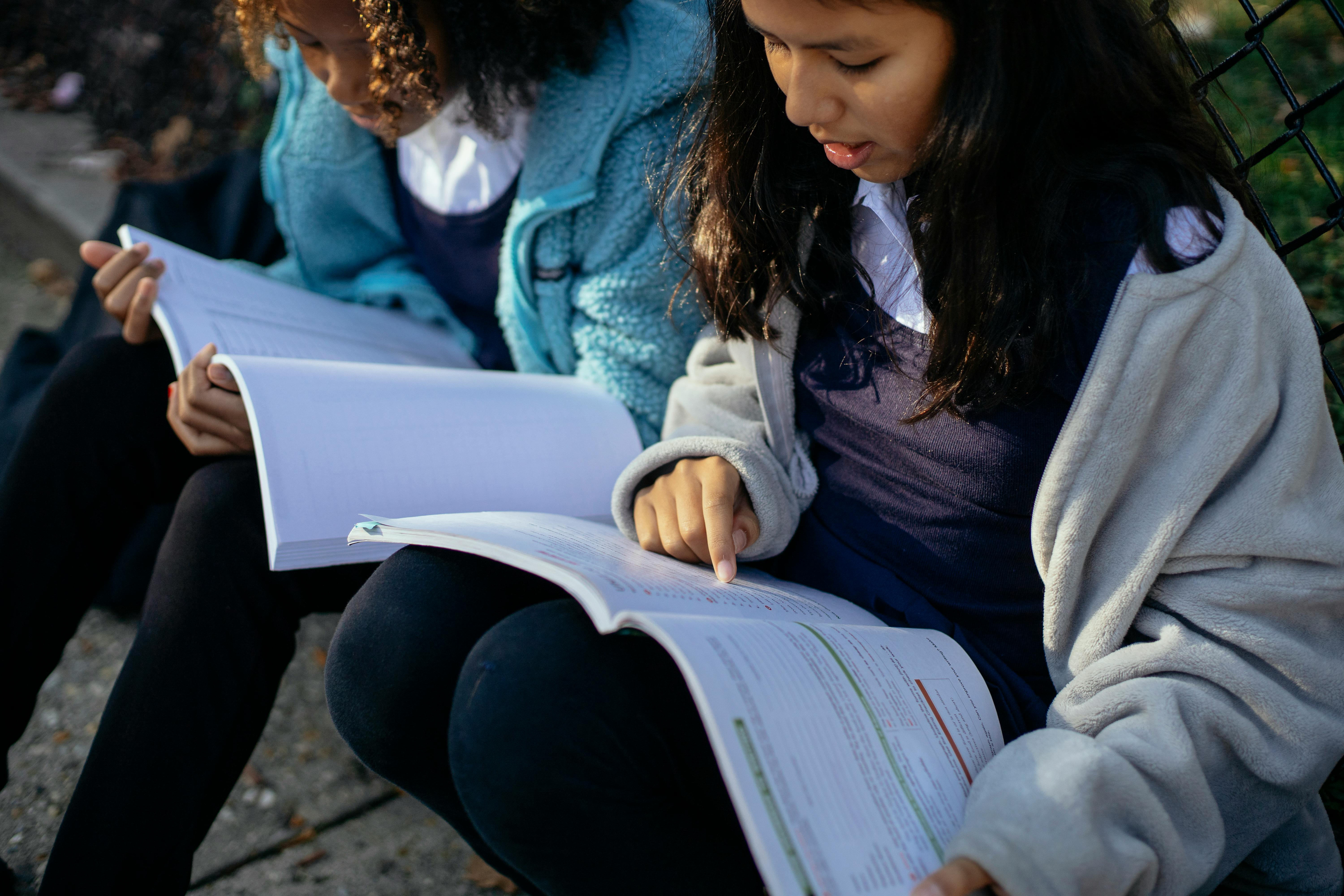 crop concentrated schoolgirls reading textbook in park