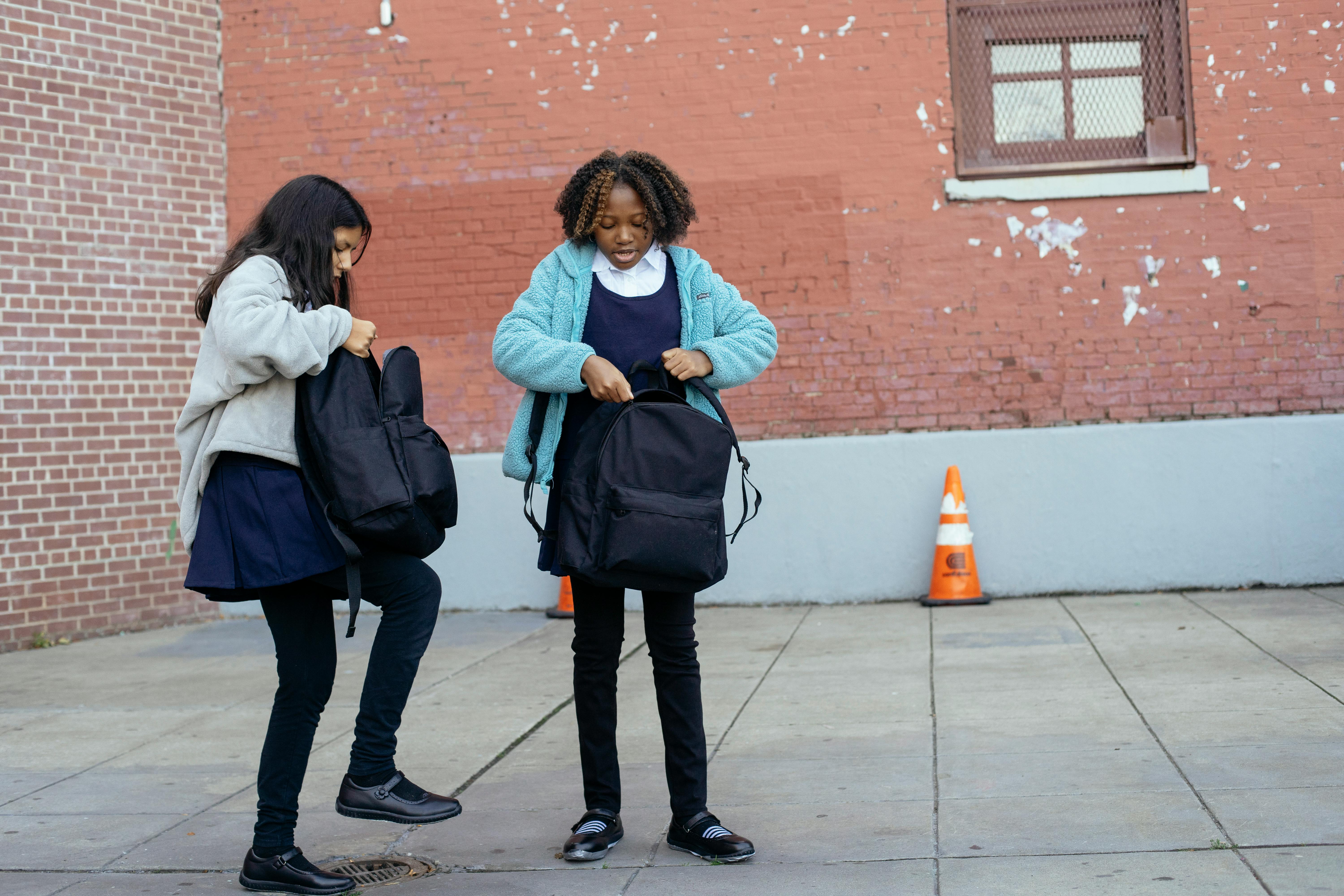 multiethnic schoolgirls standing outside school and closing backpacks