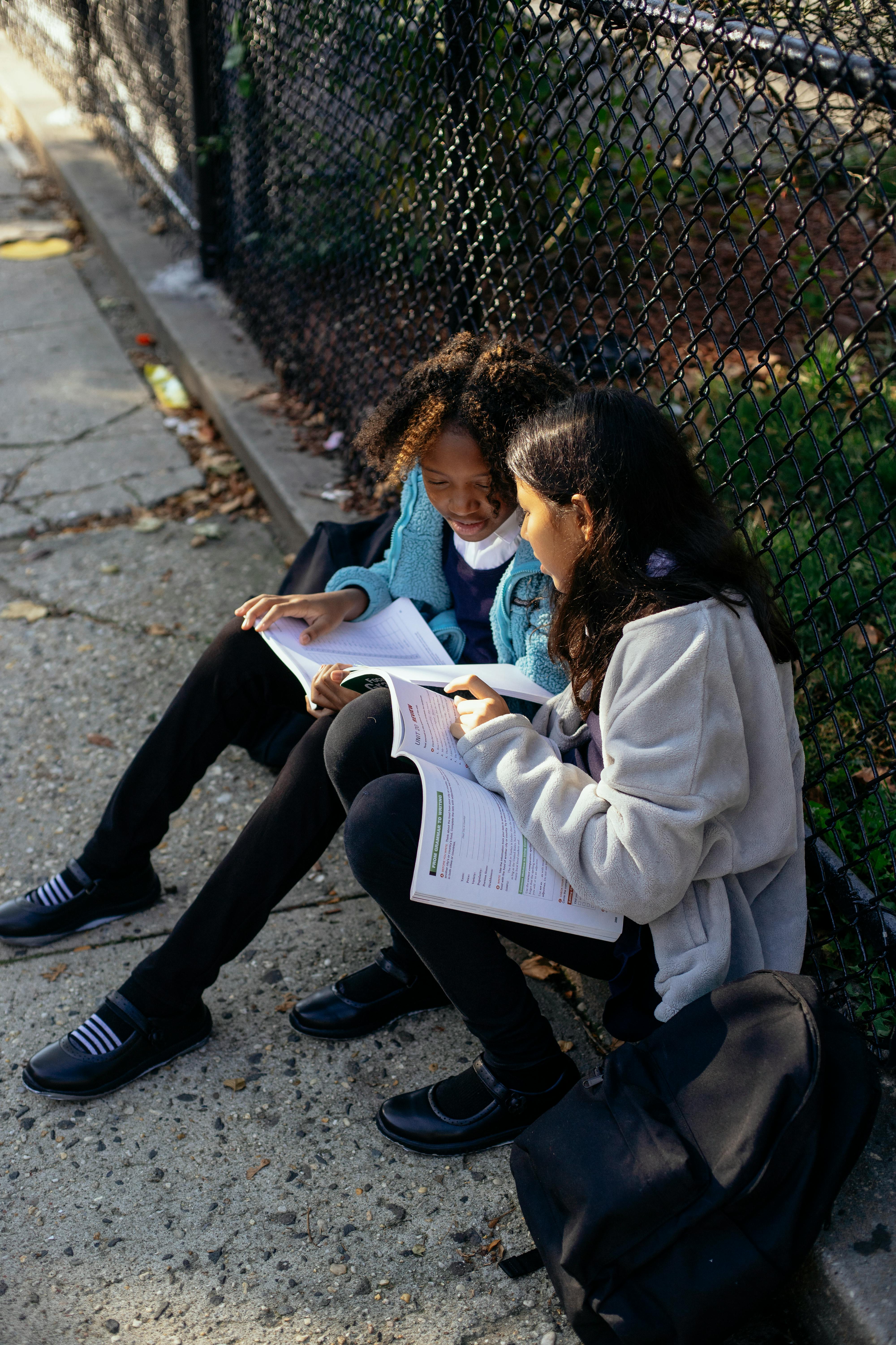 diligent multiethnic schoolgirls reading textbooks in autumn park