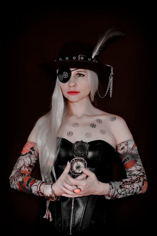 Serious female with eye patch and hat wearing pirate carnival outfit standing with compass against black background