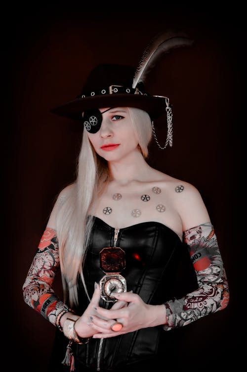 Creative female wearing hat and black corset with pirate eye patch standing with compass and looking at camera