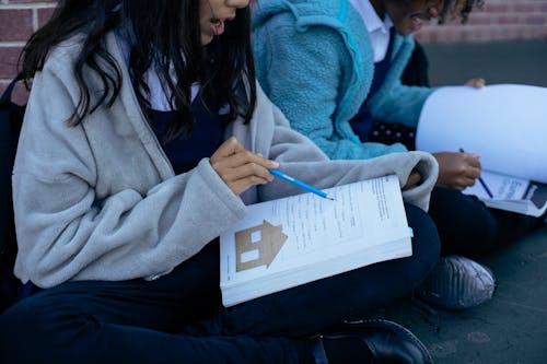 Young diverse pupils studying lesson together while sitting in yard