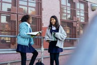 Cheerful smart multiethnic children with textbooks standing near school and talking about exam