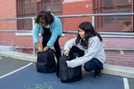 Adorable multiracial children touching backpacks while talking about education near old building of school