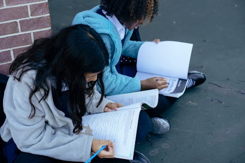 Ragazze Multietniche Intelligenti Che Scrivono E Fanno I Compiti Nei Libri Di Testo