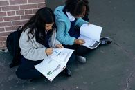 From above of adorable diligent pupils learning and reading textbooks while sitting near brick wall