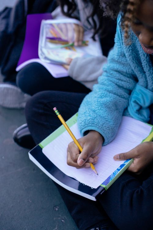 Free Crop cute intelligent African American pupil doing homework with pencil on sheet of paper on blurred background Stock Photo