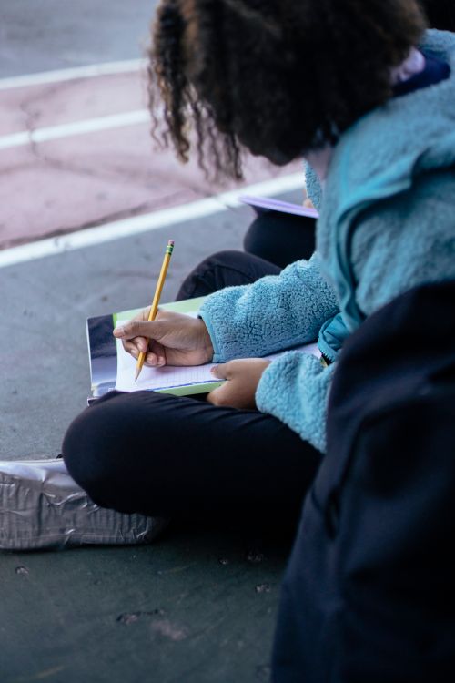 Free Side view of crop anonymous intelligent African American girl doing lessons with pencils on ground Stock Photo