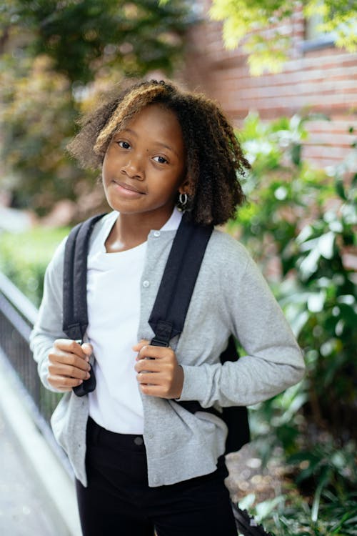 Cheerful adorable African American girl smiling and looking at camera on blurred background of street