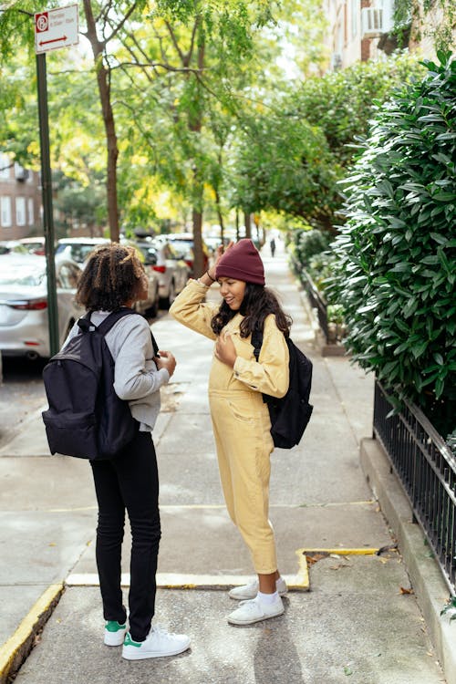 Stylish little girlfriends standing on sidewalk of street