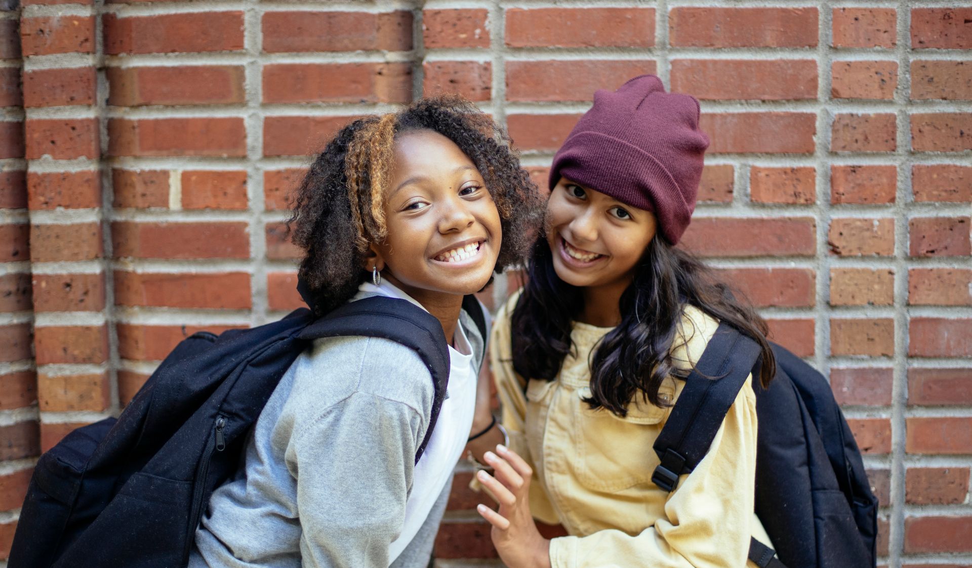 Happy black schoolkid with Afro hairstyle standing close to content best Hispanic friend while looking at camera on street