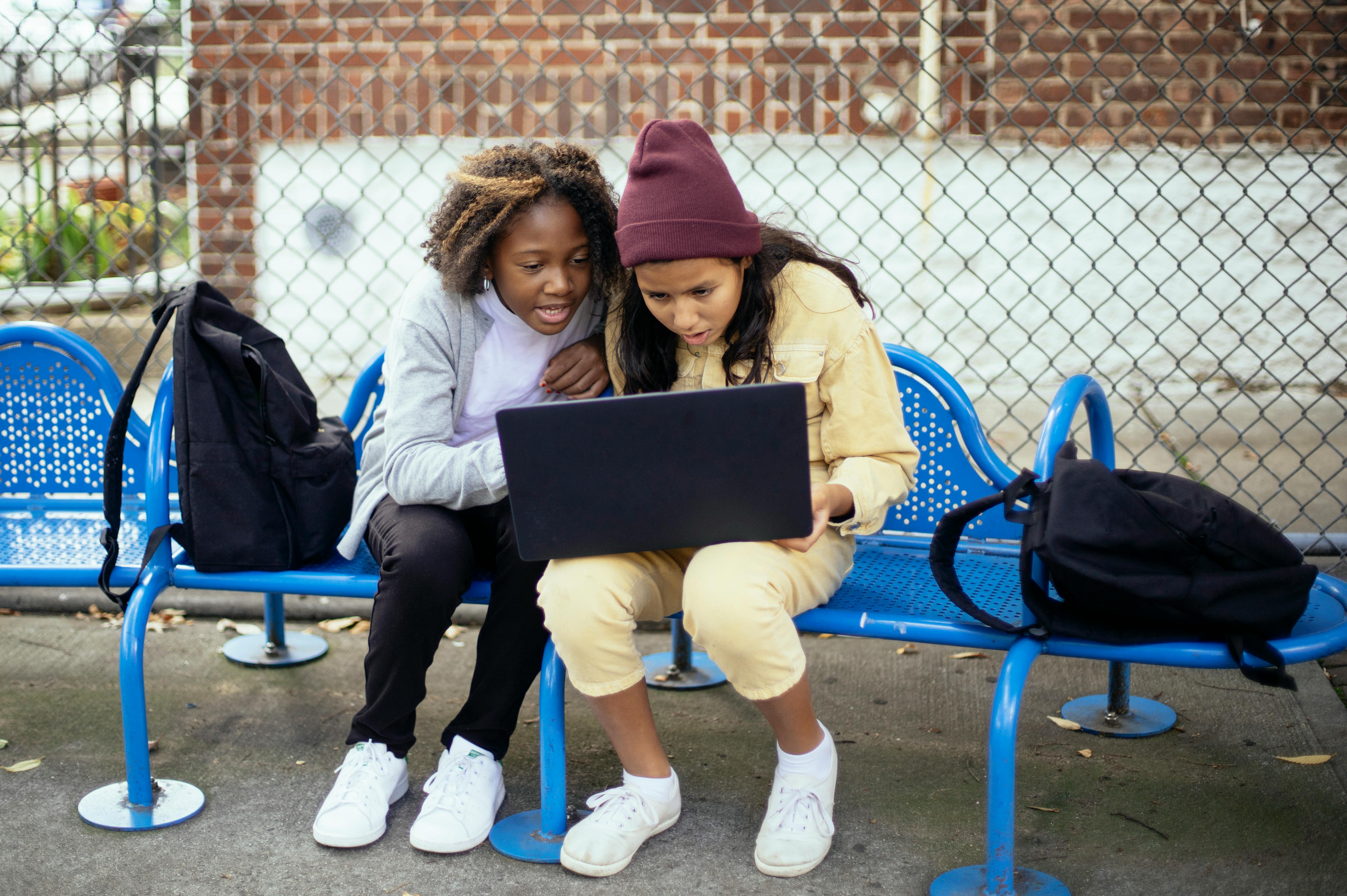 surprised multiethnic schoolchildren watching laptop on urban bench