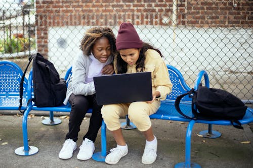 Surprised multiethnic schoolchildren watching laptop on urban bench
